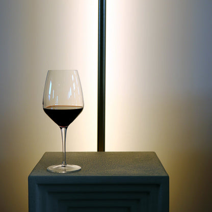 Atelier Cabernet wine glass filled with red wine standing on a white surface and a long lamp in the background