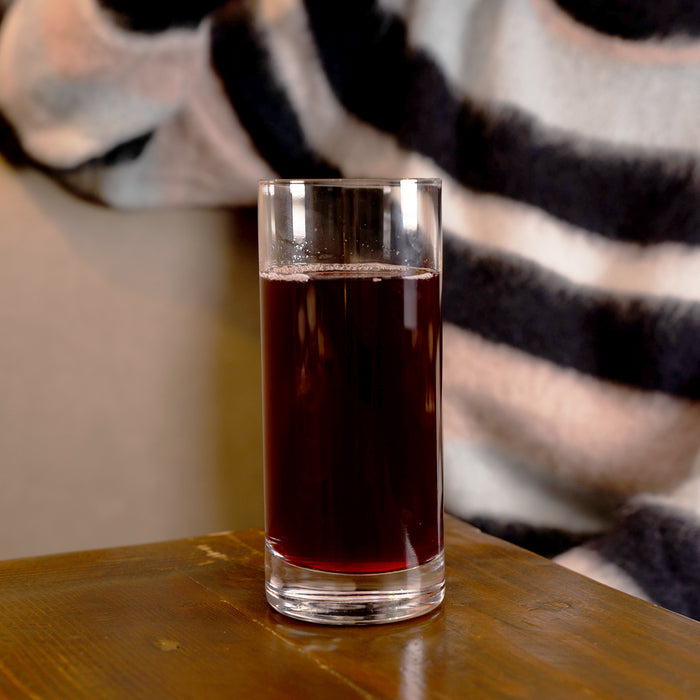 Classico Highball Glass filled with pomegranate juice and standing on a wooden surface and a person with a striped sweater in the background