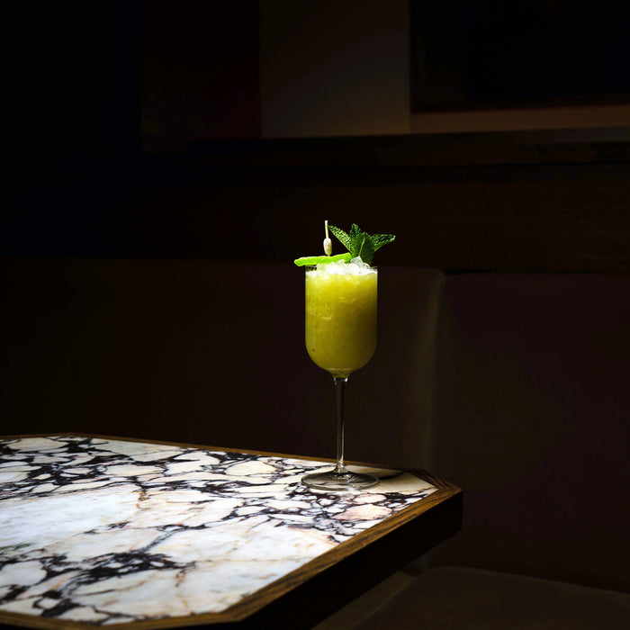 Jazz Negroni Cocktail Glass filled with bright green cocktail and garnished with mint leaves standing on a marble surface and a dark background