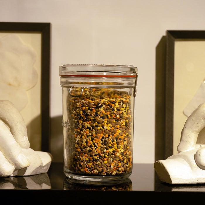 Lock-Eat jar filled with legumes standing on a black reflective surface and frames and hand sculptures in the background
