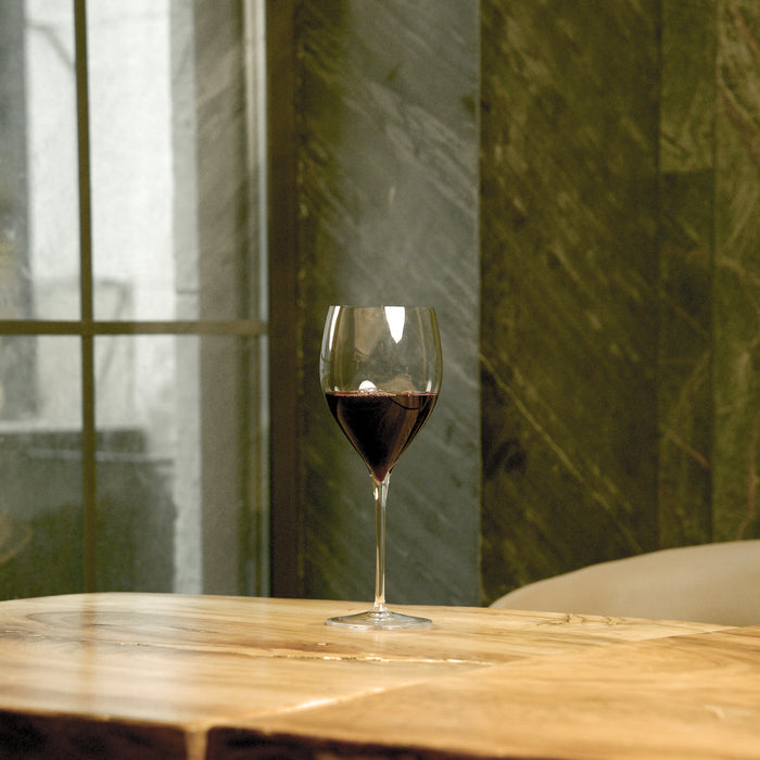 Magnifico large wine glass filled with red wine standing on a wooden table and a dark green background