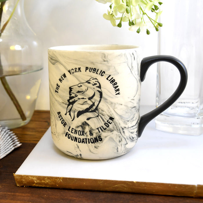 White marbleized mug with vintage NYPL lion logo in black on a night table.