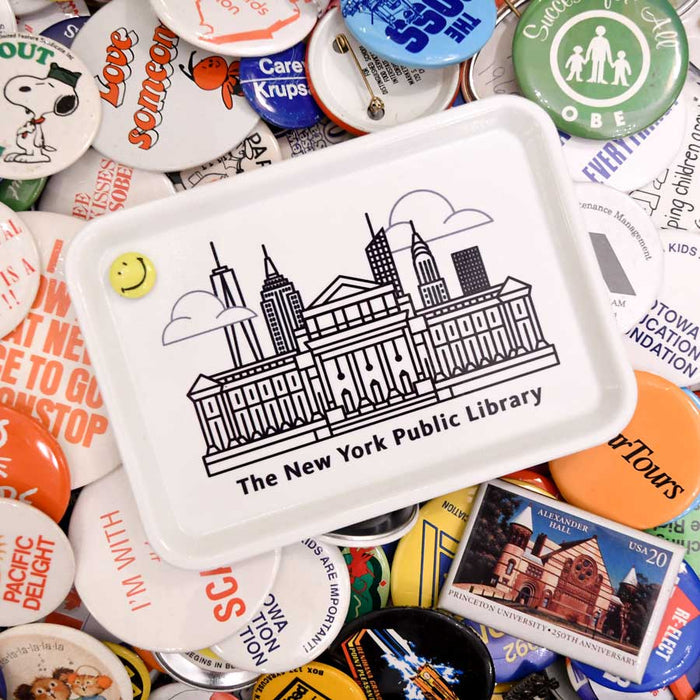 A white rectangular fiberglass tray with an illustration of The New York Public Library building and the New York City skyline in black on a colorful pins background.