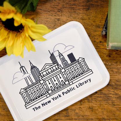 A white rectangular fiberglass tray with an illustration of The New York Public Library building and the New York City skyline in black on a wooden table.