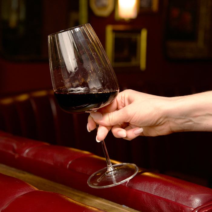 Hand holding Optica Bordeaux glass filled with red wine on a dark background