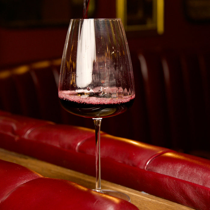 Optica Bordeaux glass filled with red wine on a dark background