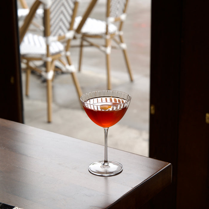 Cocktail in a Optica Martini glass on a bar with chairs and a window in the background