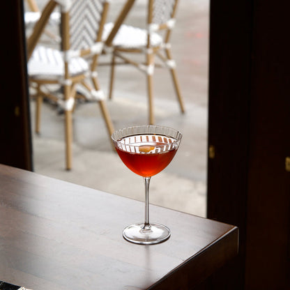 Cocktail in a Optica Martini glass on a bar with chairs and a window in the background