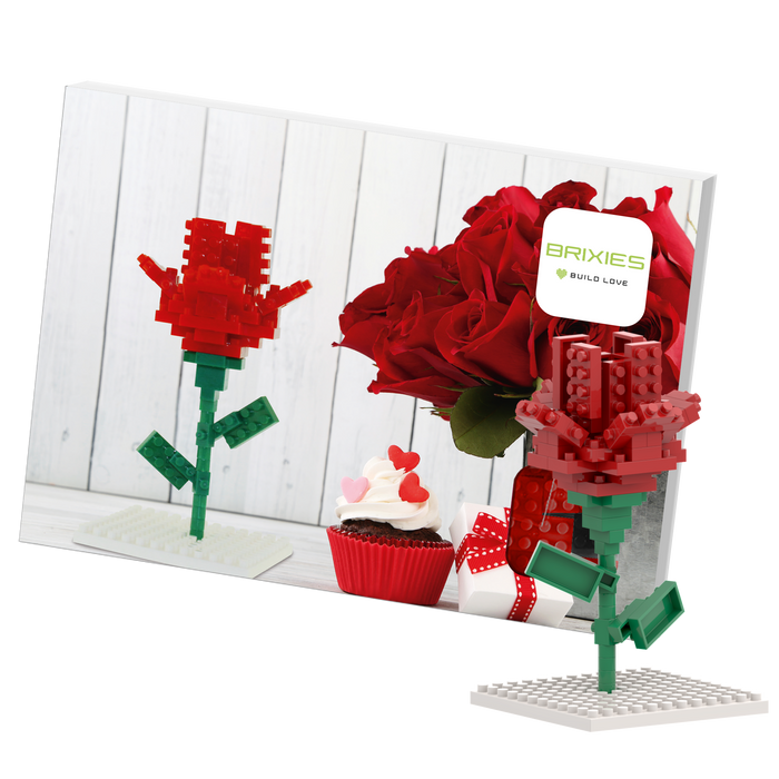 A photo shows the Brixies Postcard Flower, a LEGO-style 3D rose model, standing before a card with real red roses, a heart-decorated cupcake, and a ribboned gift box. The card features the Brixies Build Love logo.