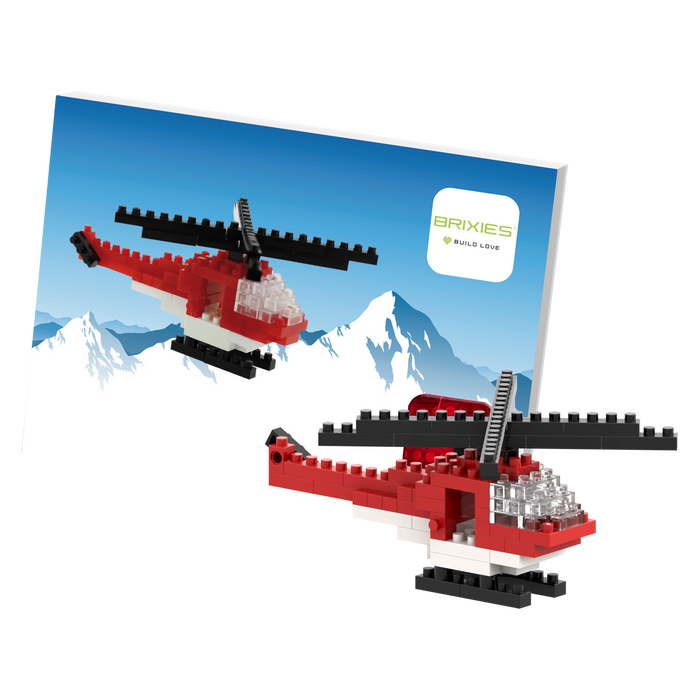 Two small red and white Brixies Postcard Helicopter models built from micro bricks are displayed in front of a postcard showing snowy mountains with the Brixies logo in the top right corner.