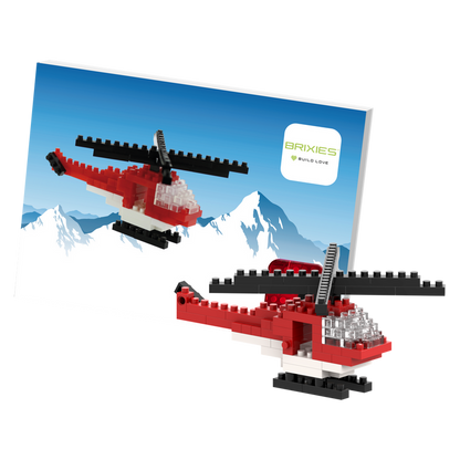 Two small red and white Brixies Postcard Helicopter models built from micro bricks are displayed in front of a postcard showing snowy mountains with the Brixies logo in the top right corner.