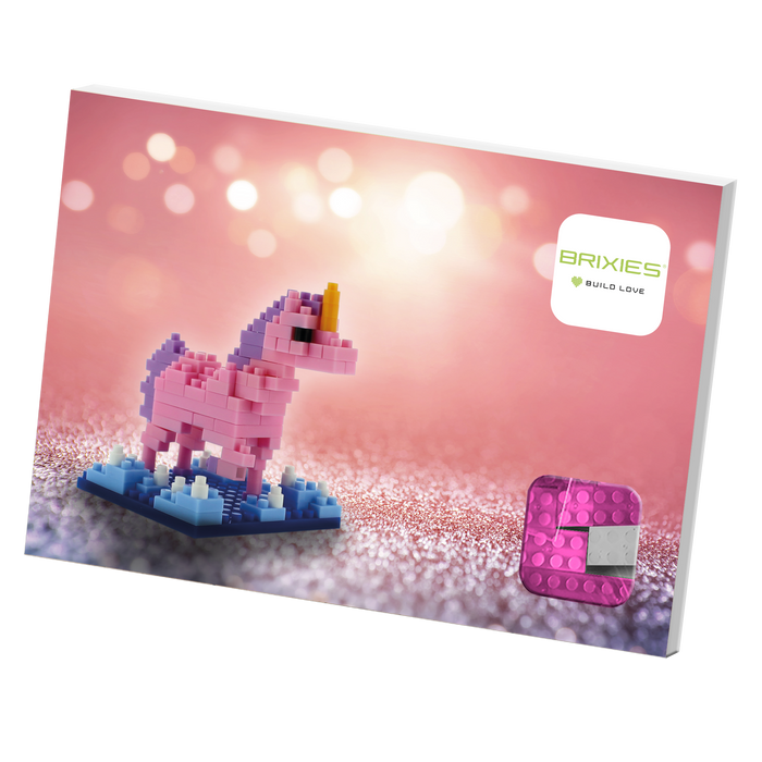 The Brixies Postcard Unicorn features a pink and purple unicorn micro brick kit, set against a sparkling pink background with the Brixies logo and a pink building block in the lower right corner.