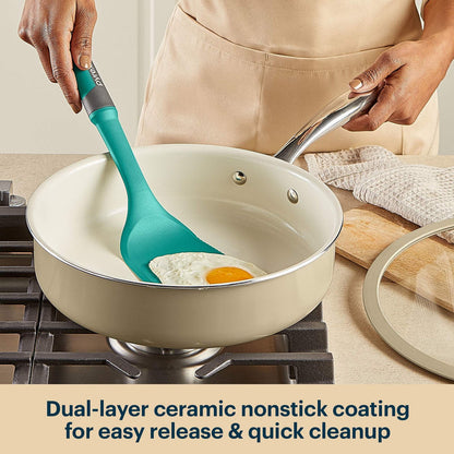 Person using a green spatula to stir eggs in a beige ceramic nonstick frying pan on a stove.
