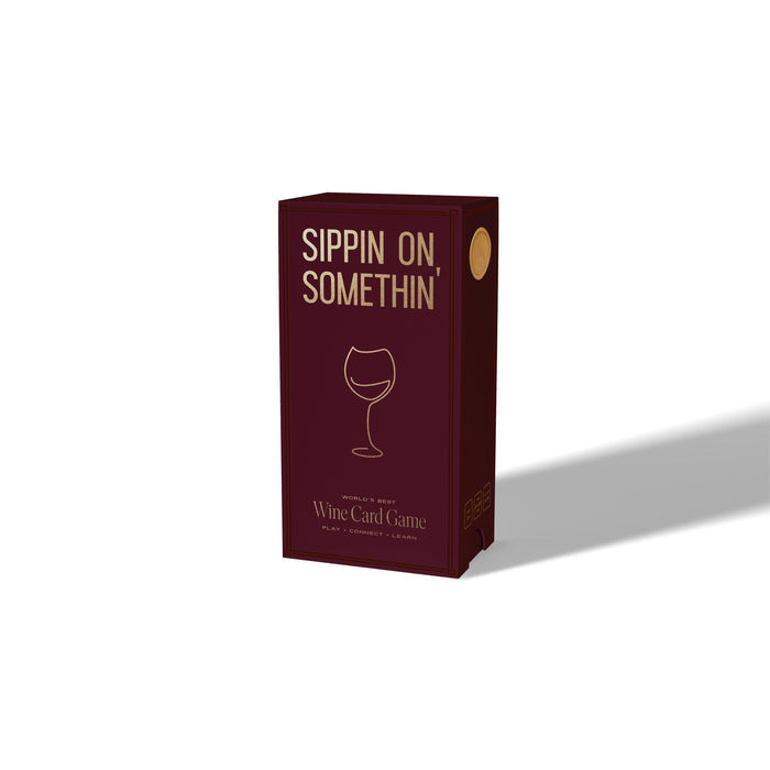 A burgundy box from Som Ventures, labeled “Sippin on Somthin’” with a minimalist wine glass design on the front. “Wine Card Game” is written below, inviting you to play, connect, and learn fun wine trivia. The box casts a rightward shadow.