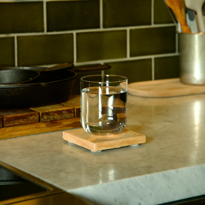 Sublime DOF glass filled with water standing on a coaster kitchen counter with various items in the background