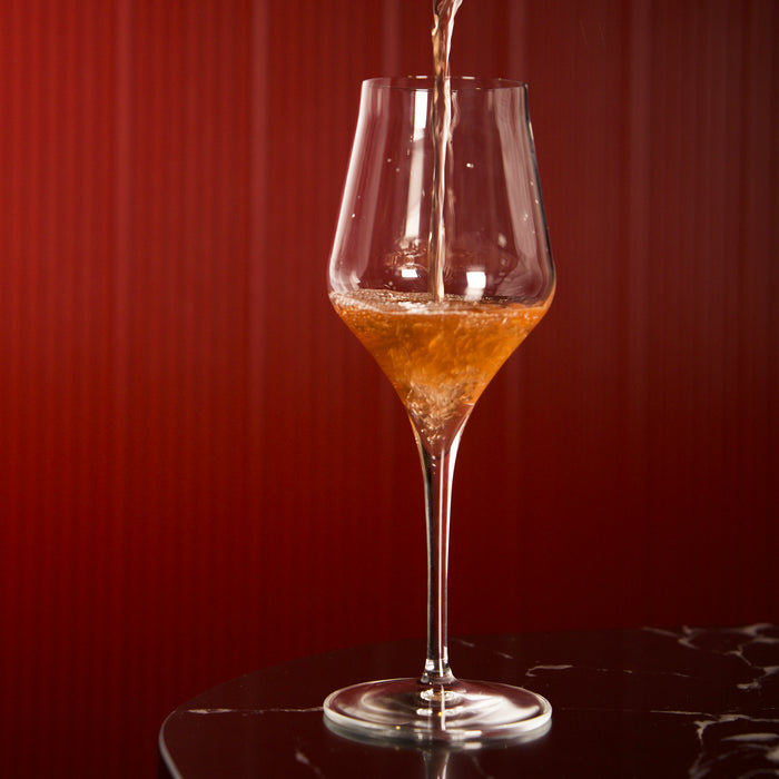 Supremo Chardonnay wine glass being filled with orange wine against a dark background