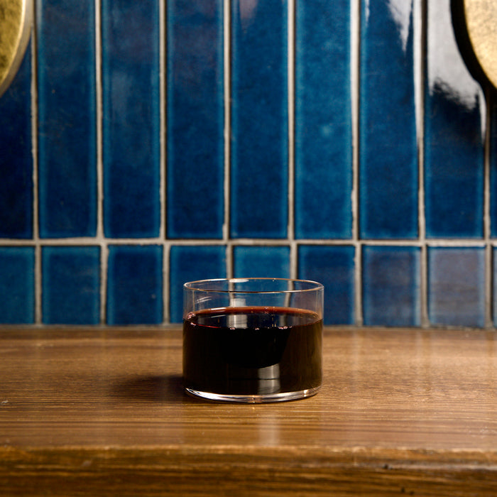 Top Class aperitivo glass filled with red wine standing on a wooden surface with a blue backsplash background