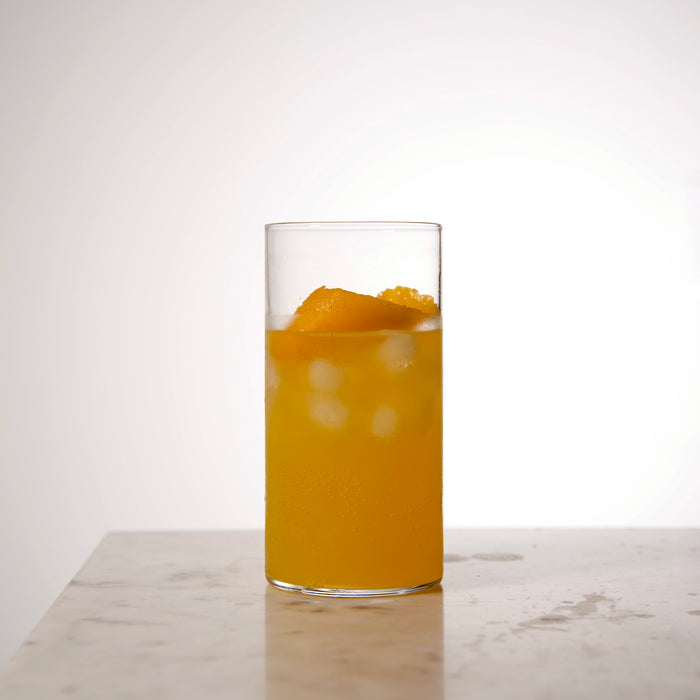 Top Class Highball Glass filled with an orange cocktail and garnished with a orange twist standing on a light marble surface and light neutral background