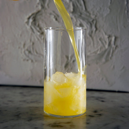 Top Class Highball Glass being filled with orange juice standing on a dark marble surface and light neutral textured background