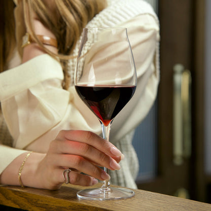 Hand holding a Vinea Cannonau wine glass filled with red wine on a soft ivory background