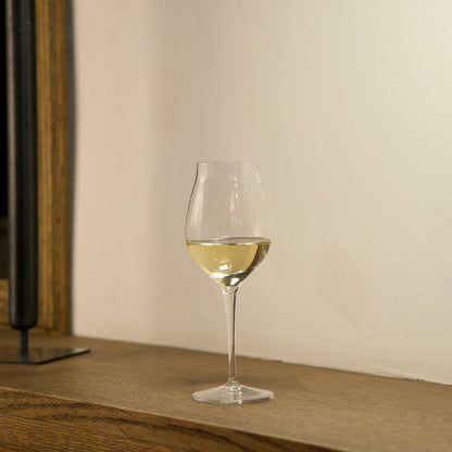 Vinea Malvasia wine glass filled with white wine on a wooden surface and a ivory background