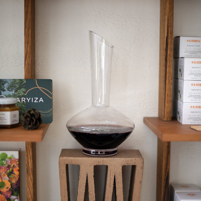 Vinea wine decanter filled with red wine standing on a side table and various items on shelves around it