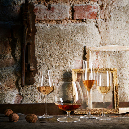 Vinoteque Cognac glass filled with a spirit standing next to other filled spirit glasses in the collection on a rustic wall background