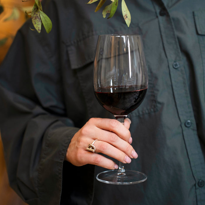 Hand holding a Vinoteque Ricco red wine glass filled with red wine on a black shirt background