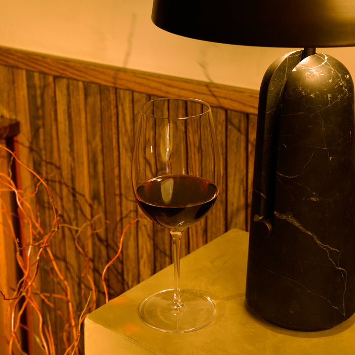 Vinoteque Riserva Red Wine glass filled with red wine and standing on a light table, wooden wall and a table lamp the background